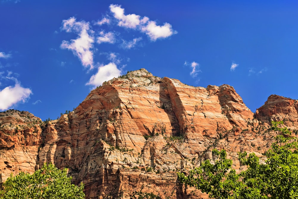 a rocky mountain with trees and clouds in the background