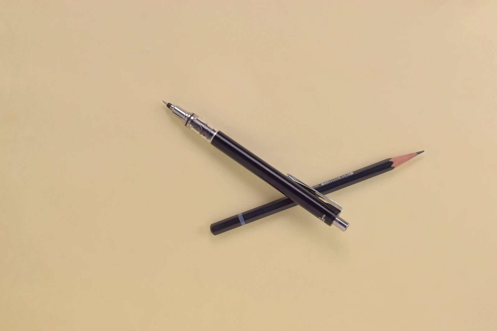Two pencils lying crossed on a warm sand-colored surface
