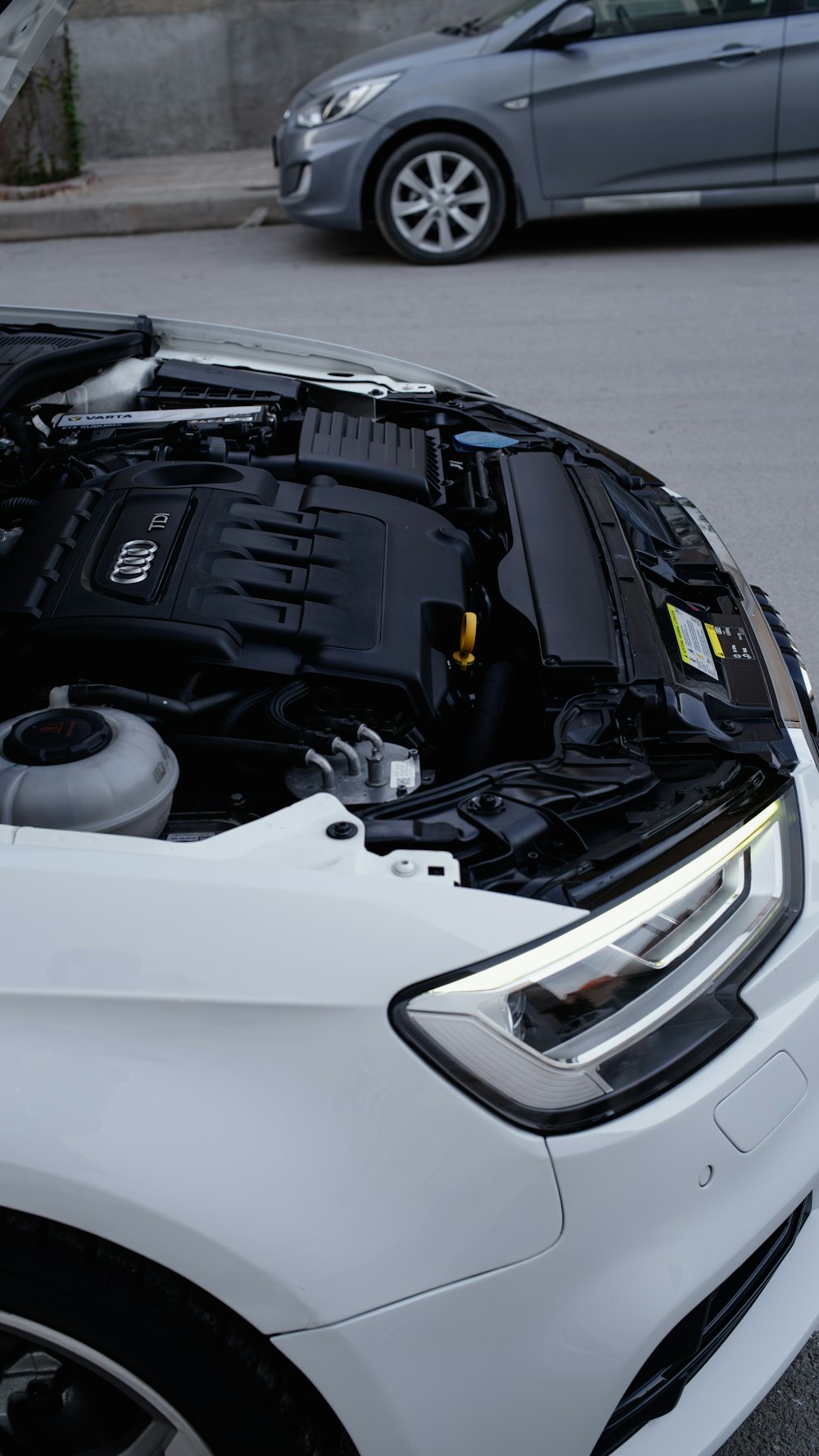 a white car with its hood open on the street