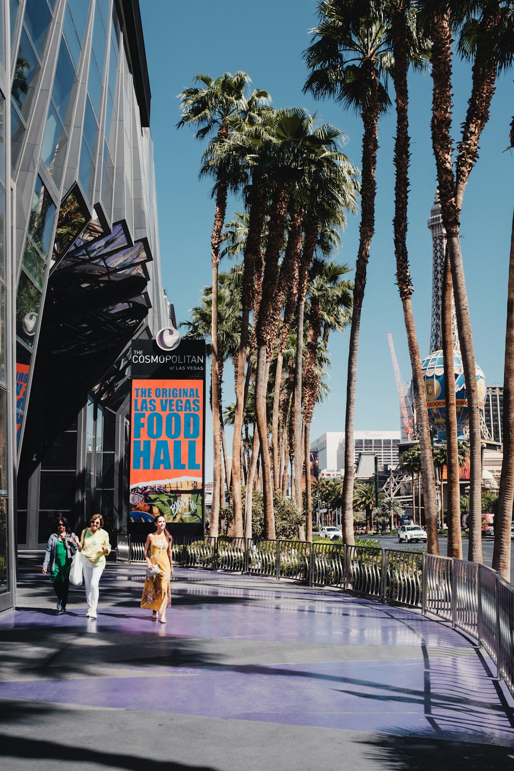 a group of people walking down a sidewalk next to palm trees