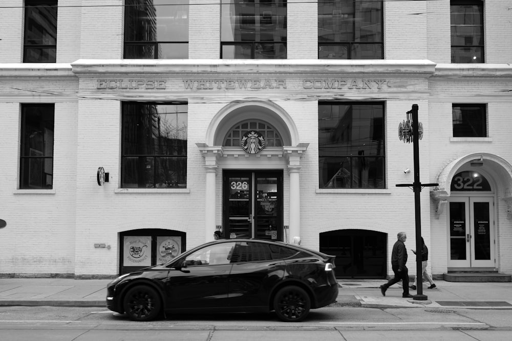 a black and white photo of a car parked in front of a building