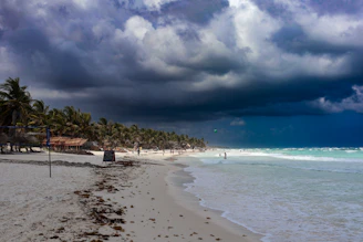 a cloudy day at the beach with people walking on the sand