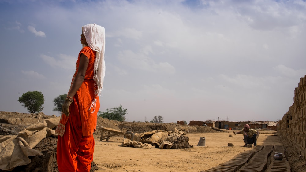 a person in an orange outfit standing in a dirt field