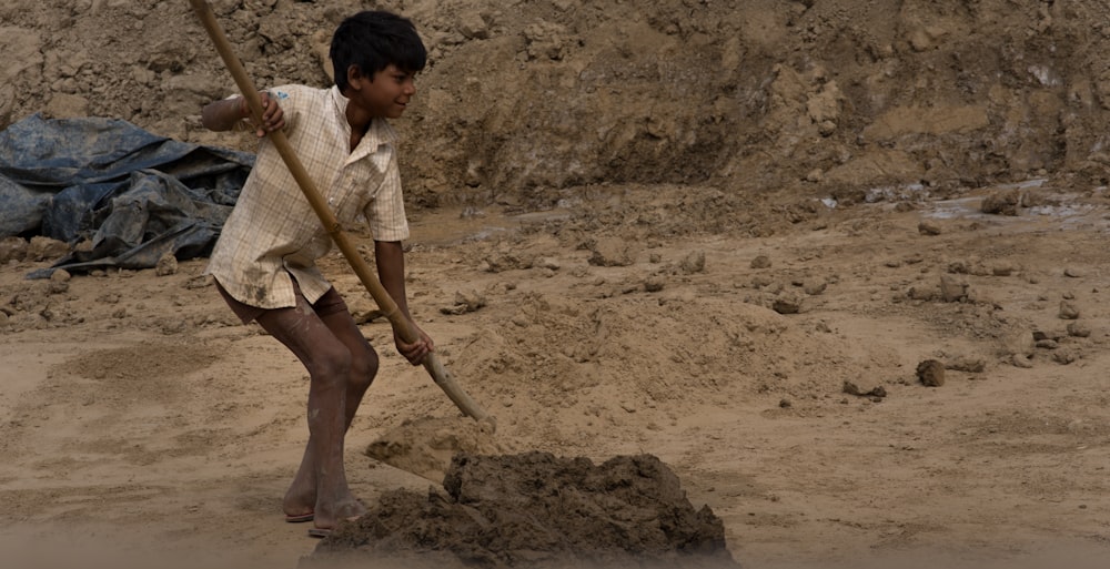 a young boy holding a stick and digging in the sand