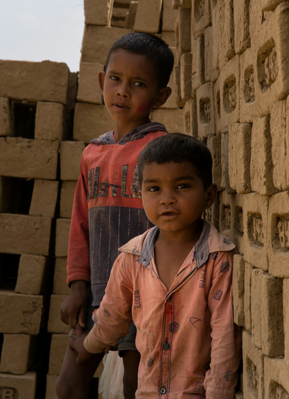 two young boys standing next to a pile of bricks