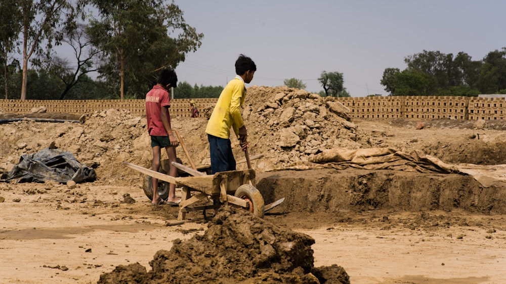 a couple of kids standing next to a pile of dirt