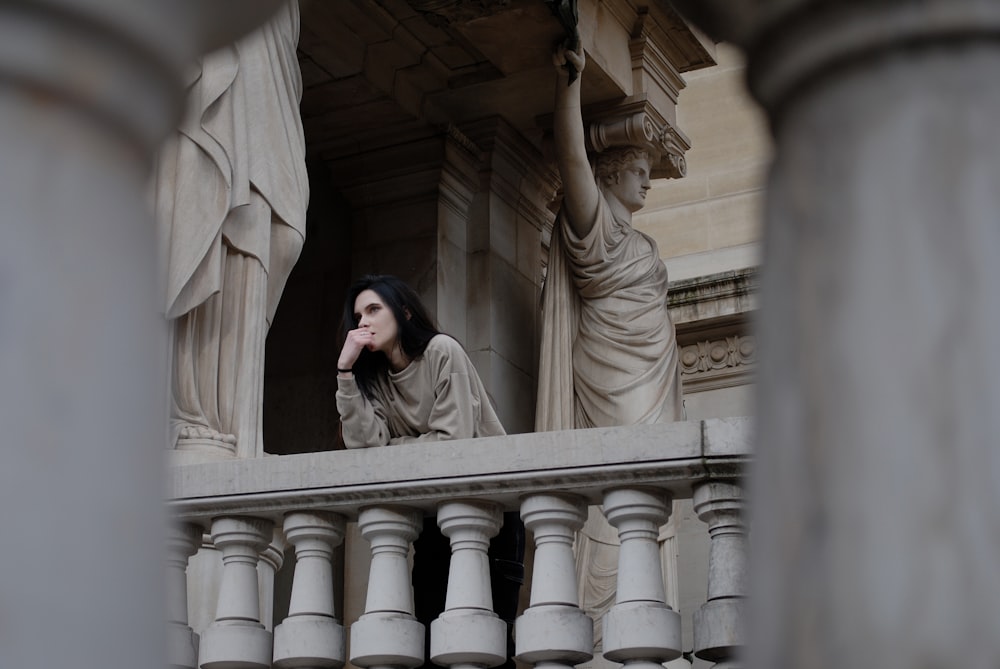 a woman sitting on a balcony with statues in the background