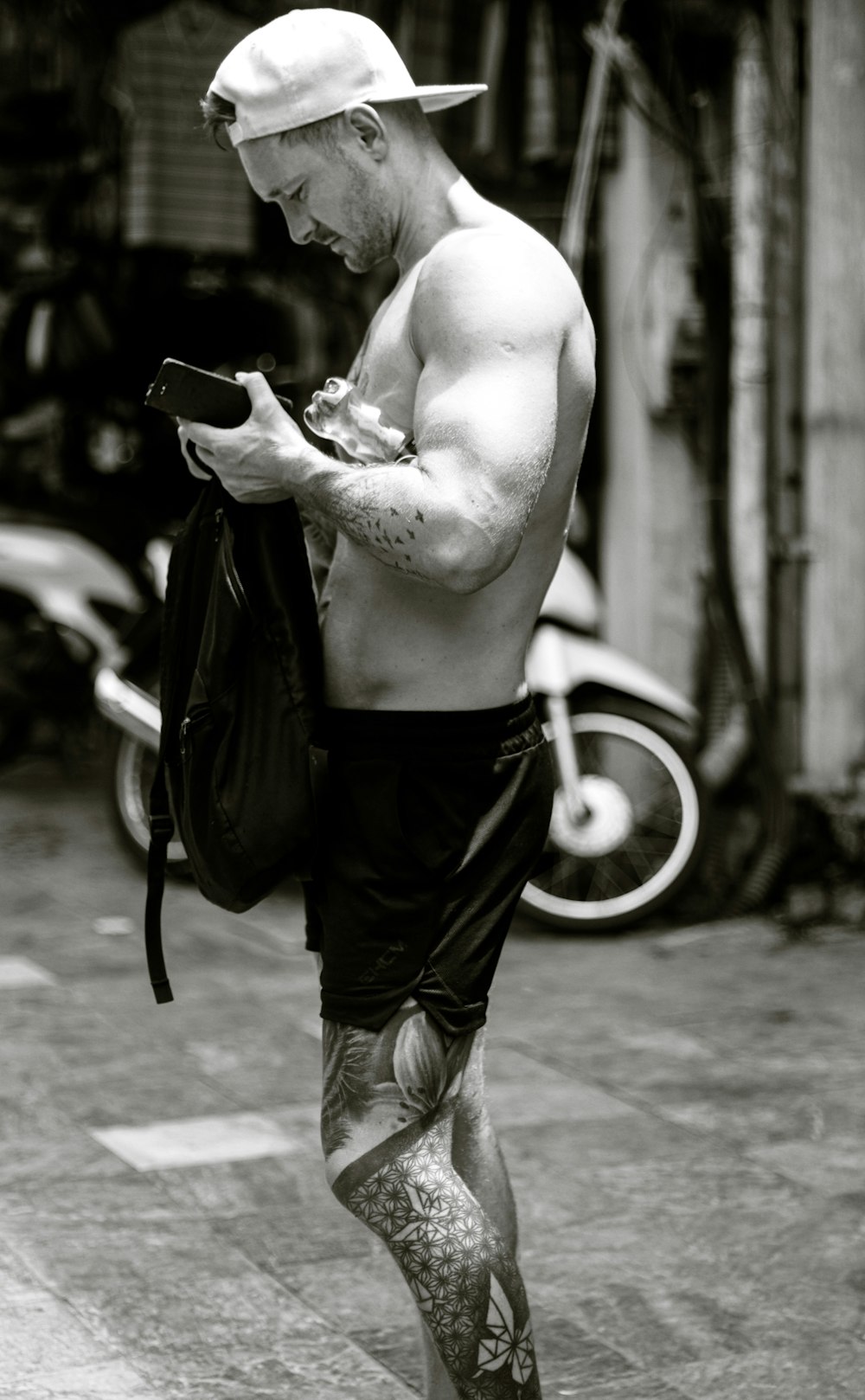 a shirtless man walking down a street while looking at his cell phone