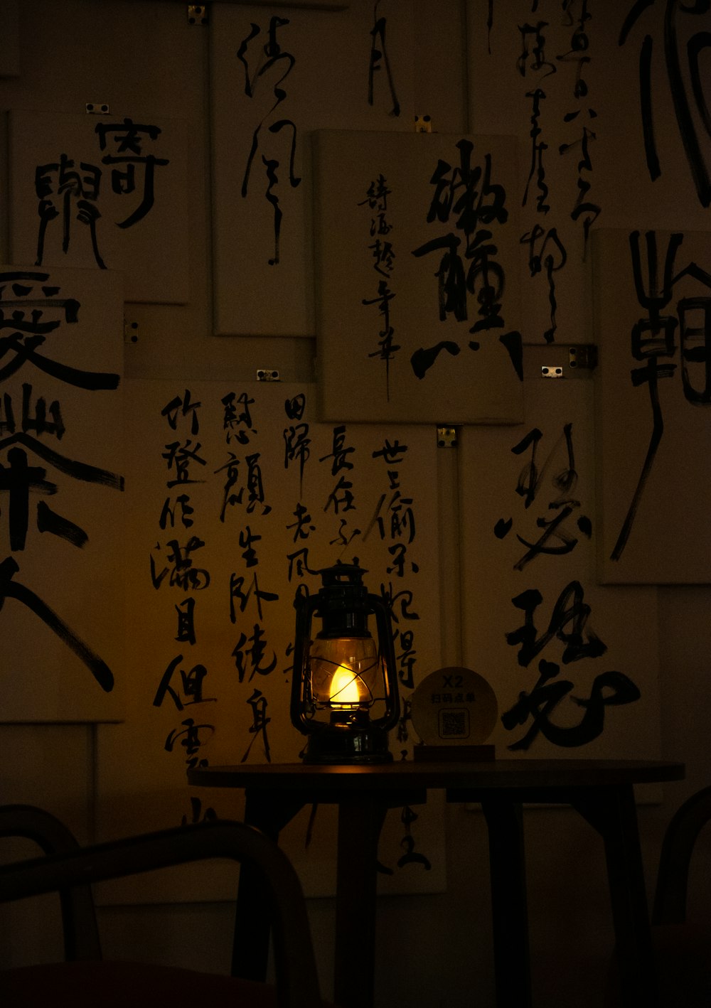 a table topped with a lit candle next to a wall covered in asian writing