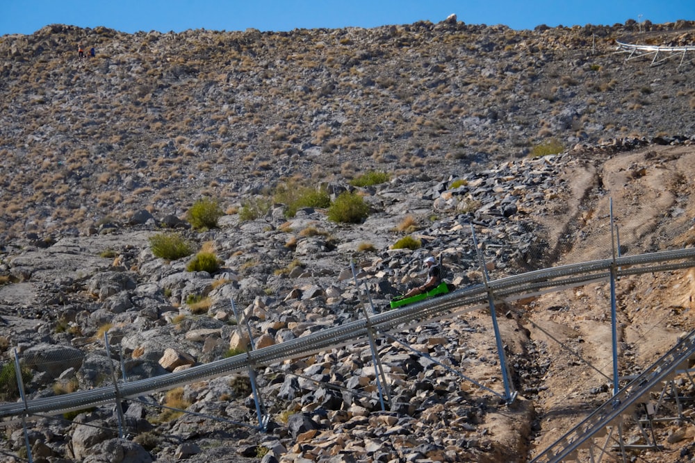 a green train traveling along a rocky hillside