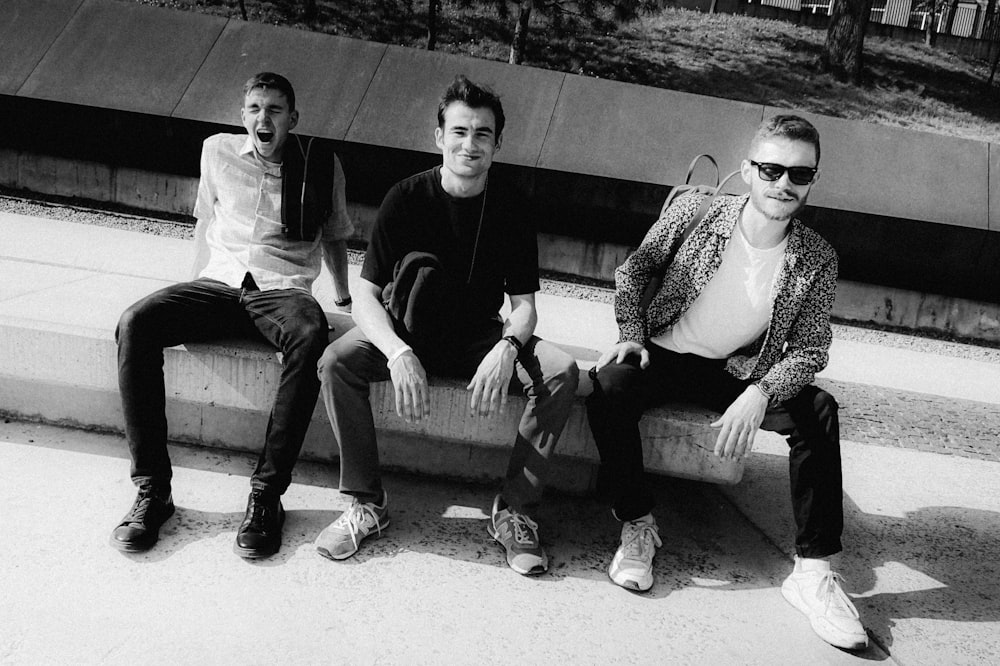 three young men sitting on a cement bench