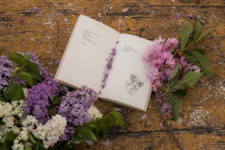 an open book sitting next to a bunch of flowers