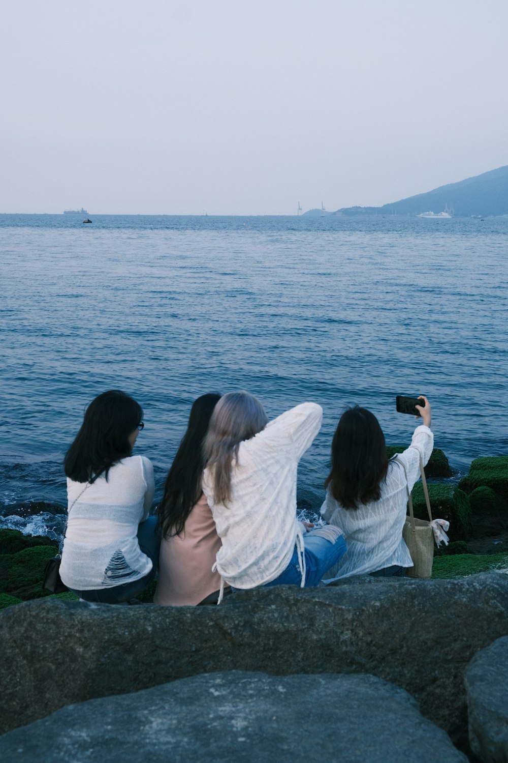 three women sitting on a rock looking out at the water