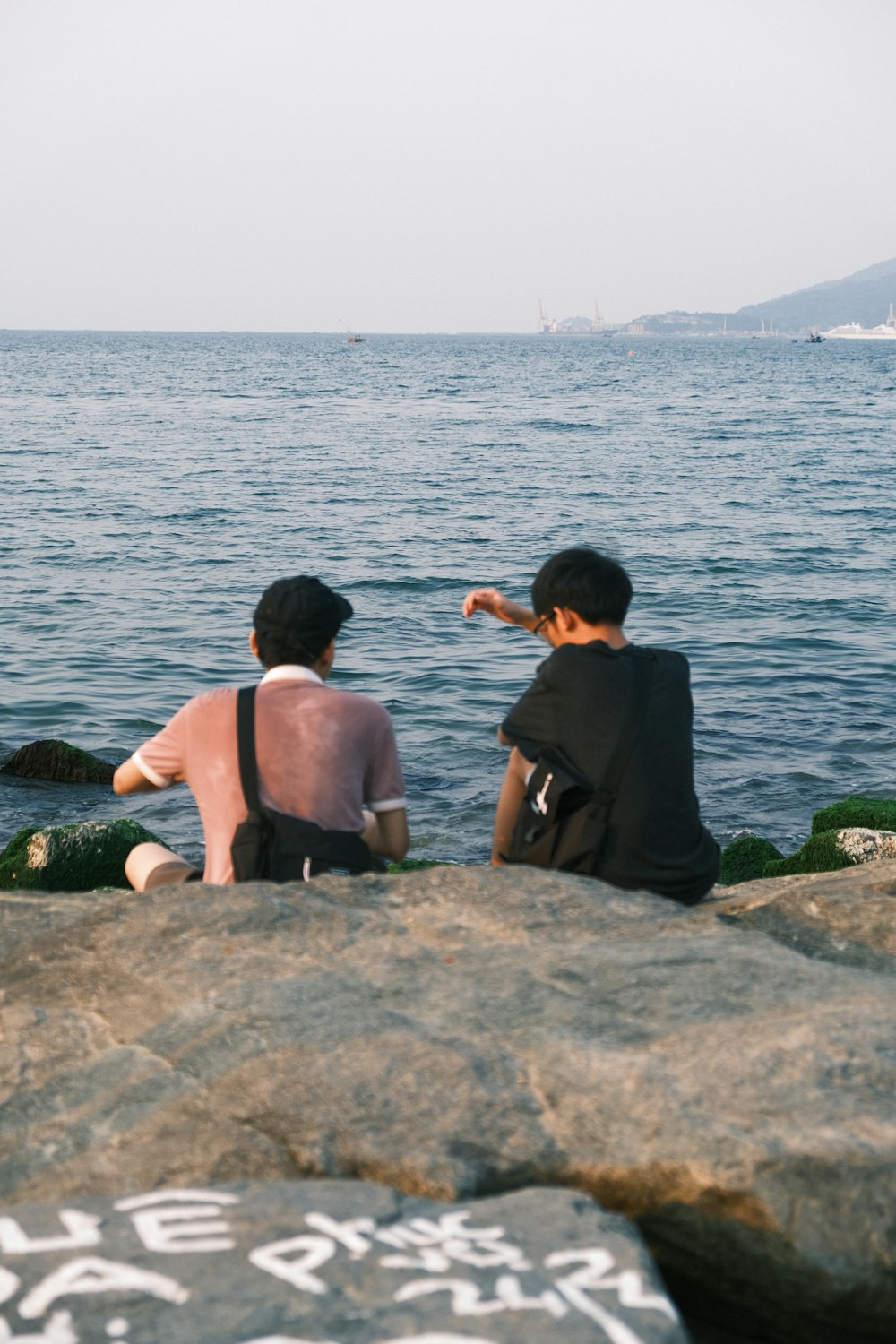 a couple of people sitting on top of a rock near the ocean