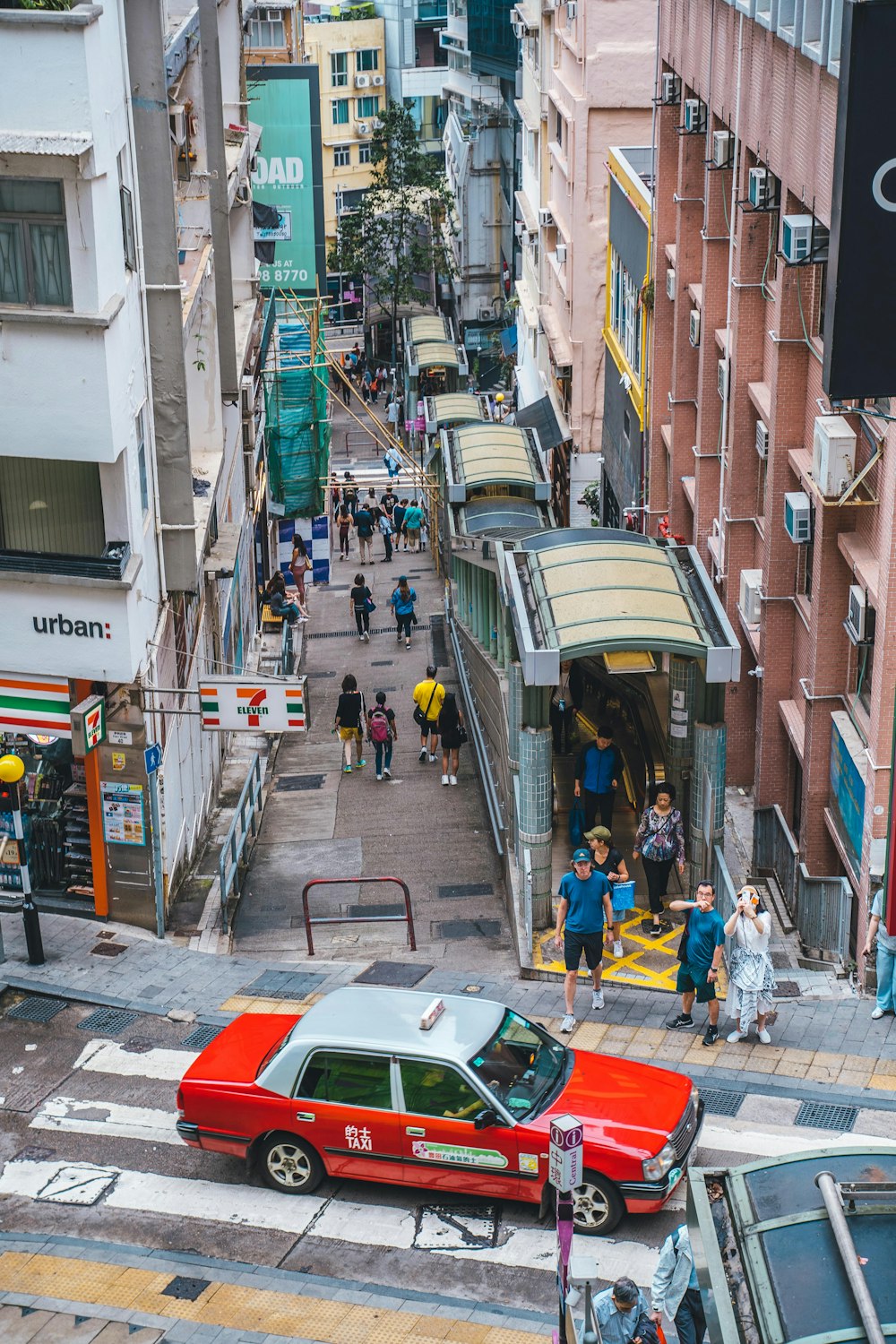 a red car driving down a street next to tall buildings