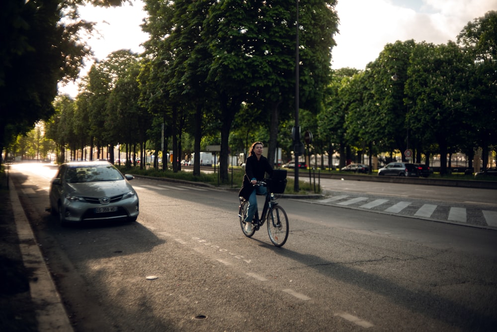 a woman riding a bike down a street next to a car