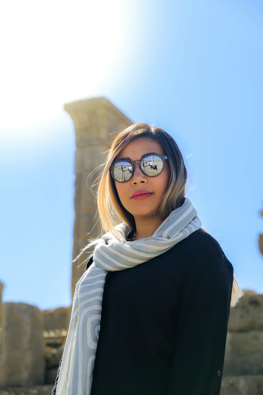 a woman wearing sunglasses standing in front of a stone structure