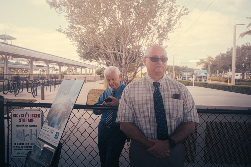 a couple of men standing next to each other near a fence