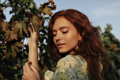 a woman with long red hair is picking leaves off a tree