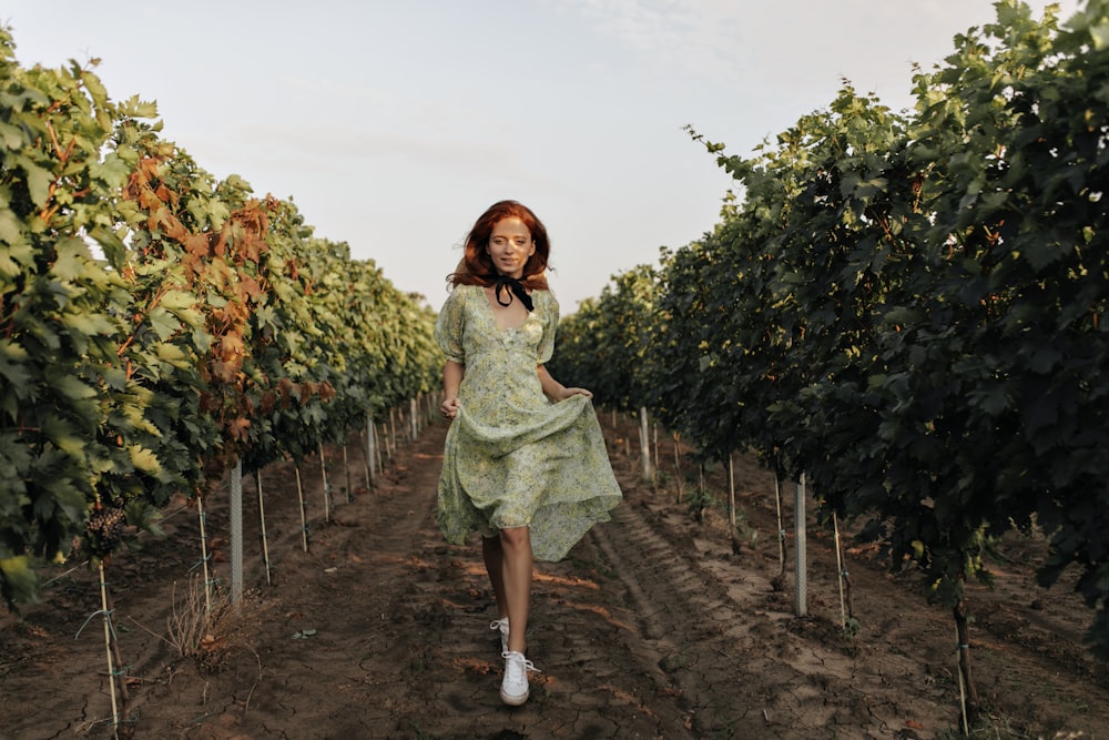 a woman in a green dress walking through a vineyard