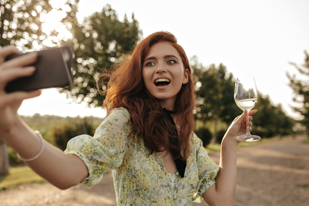 une femme tenant un verre de vin et prenant un selfie