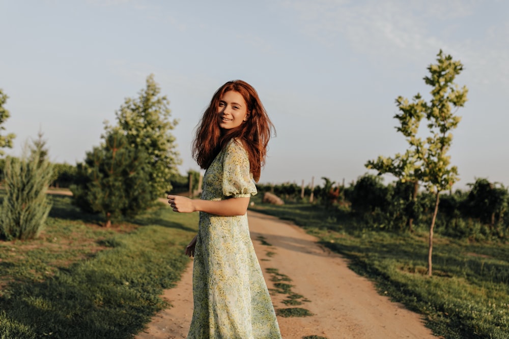 a woman in a dress walking down a dirt road