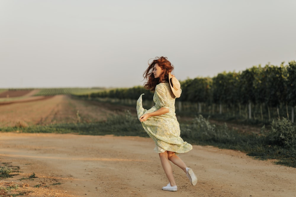 a woman in a yellow dress walking down a dirt road
