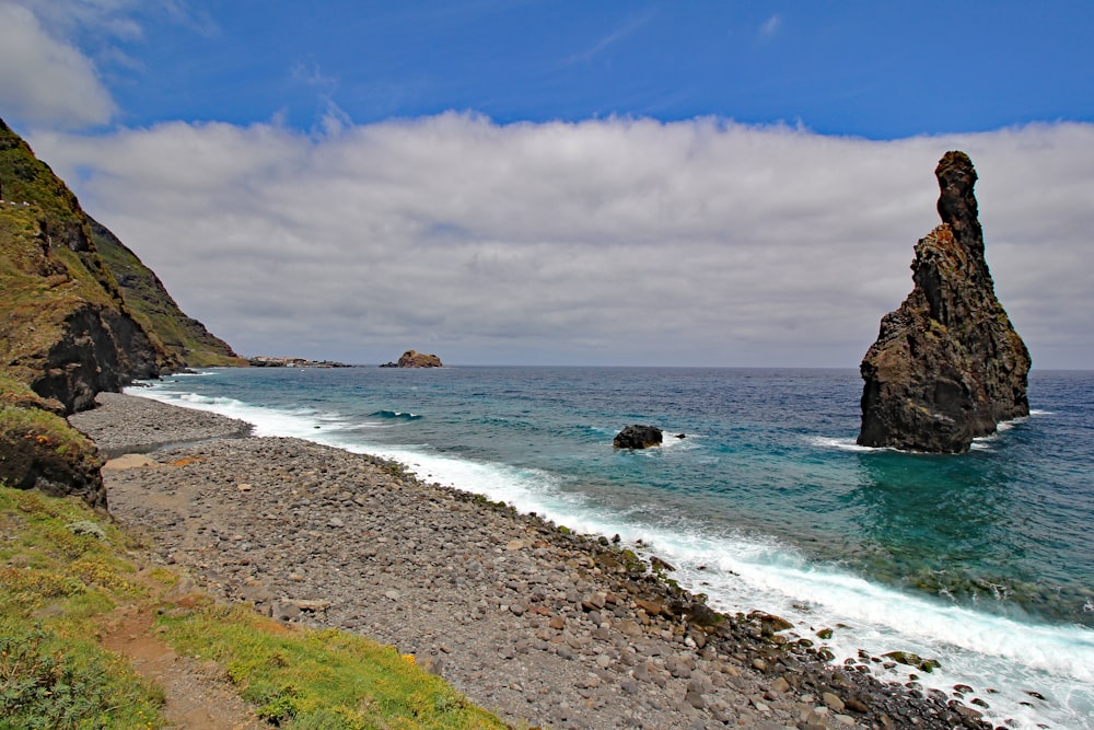 a large rock sticking out of the ocean next to a beach