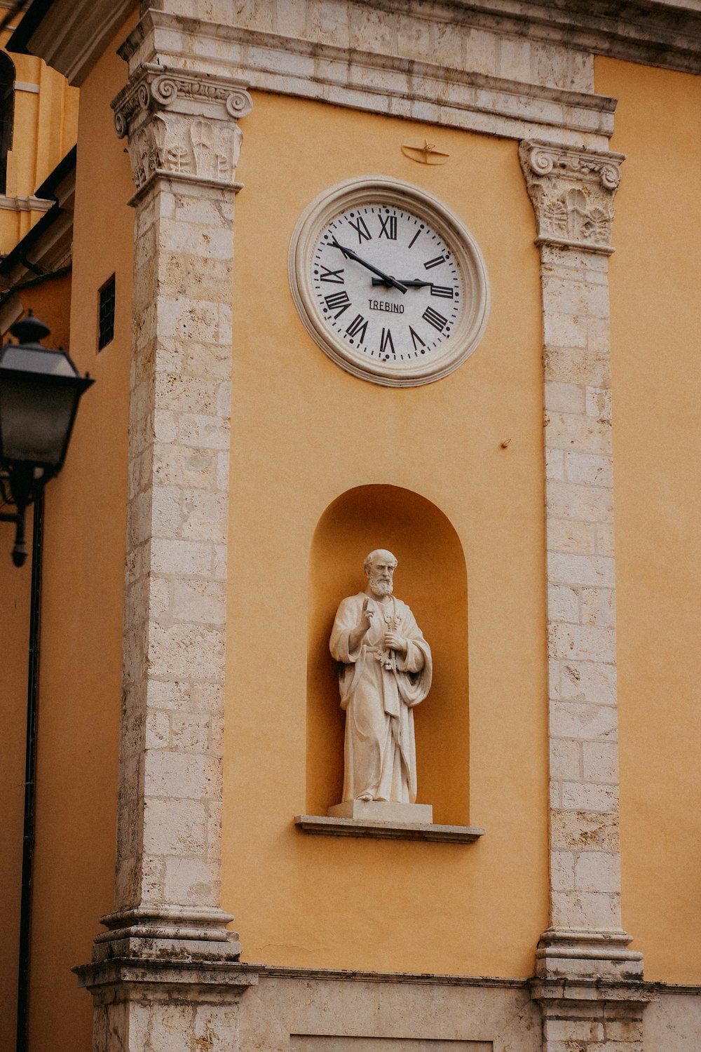 a clock on the side of a building with a statue in front of it