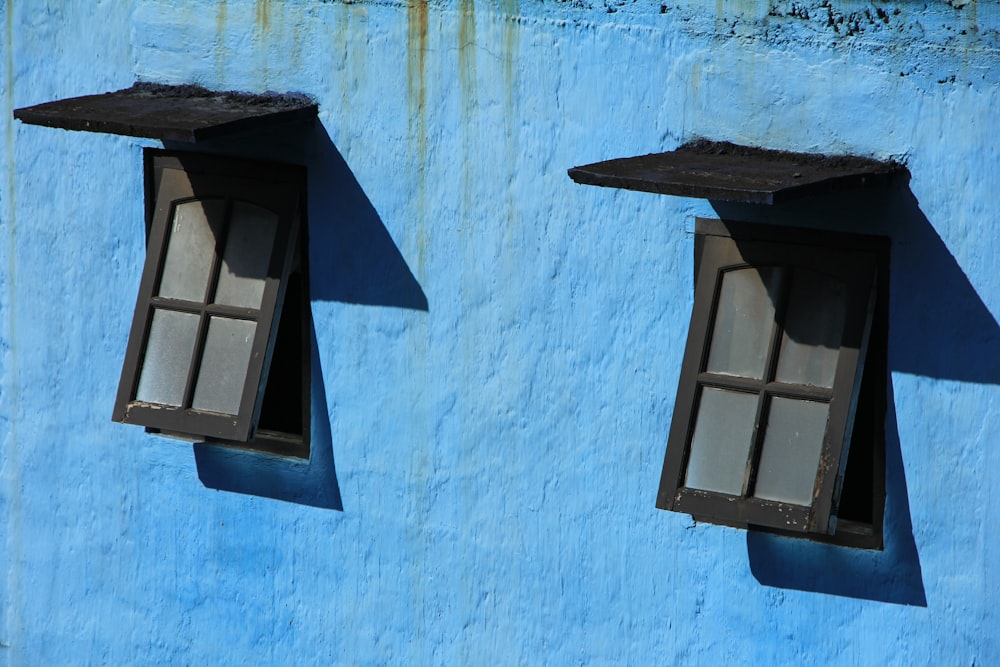 two windows on the side of a blue building