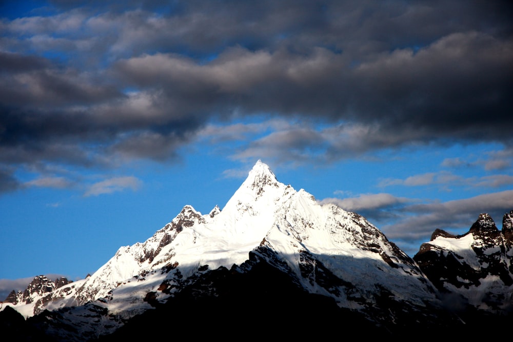 a snow covered mountain under a cloudy blue sky