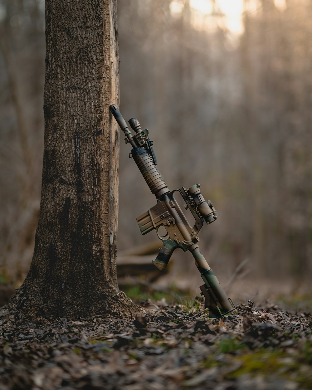 a rifle with a scope attached to a tree in the woods