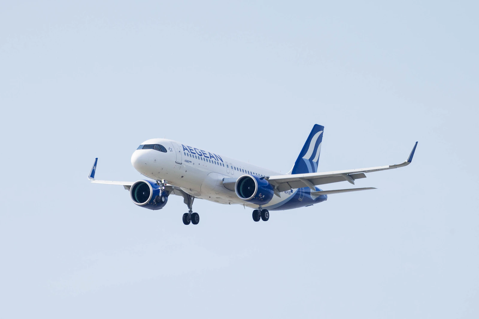 A passenger jet on final approach with its landing gear down against a clear pale sky