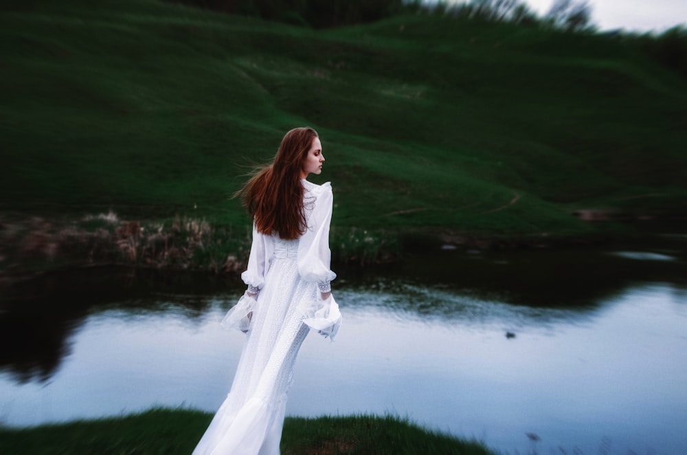 una donna in un vestito bianco in piedi davanti a uno specchio d'acqua