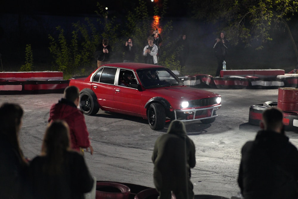 a red car driving around a track with people watching