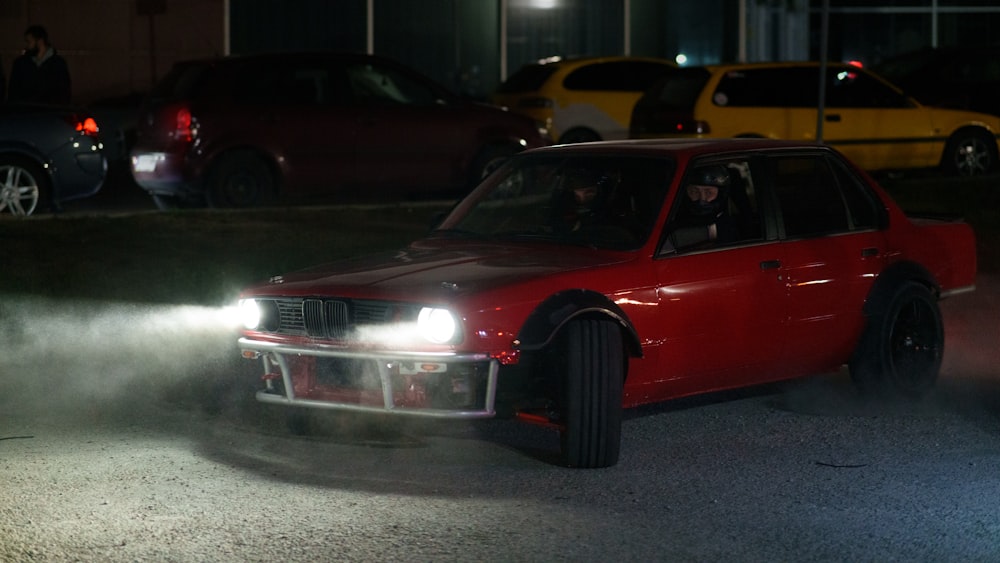 a red car driving down a street at night