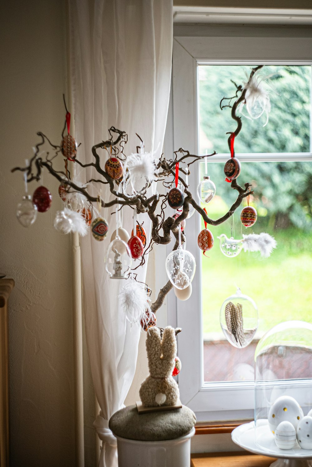 a tree with ornaments hanging from it in front of a window