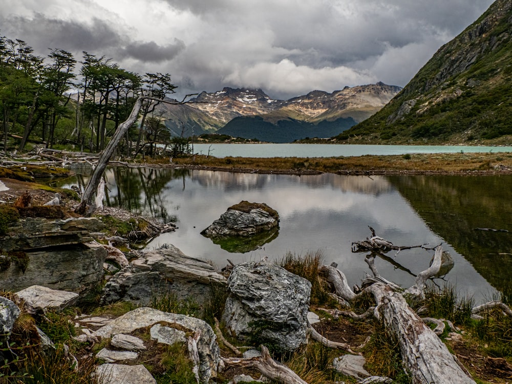 a lake surrounded by mountains and trees under a cloudy sky