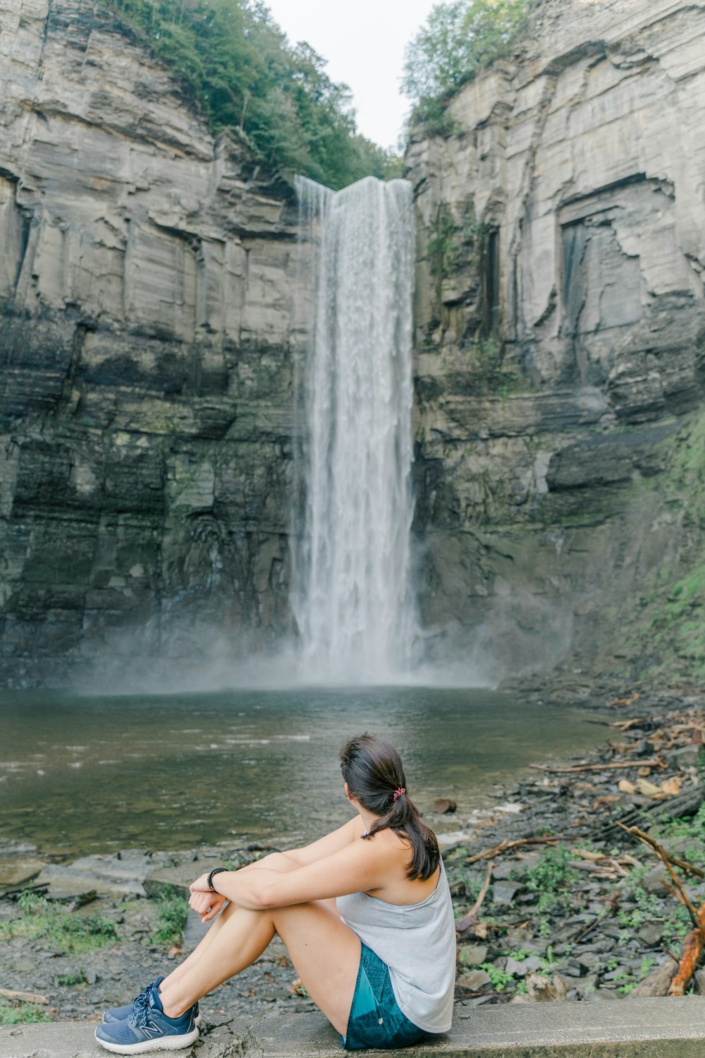 a woman sitting on a ledge in front of a waterfall