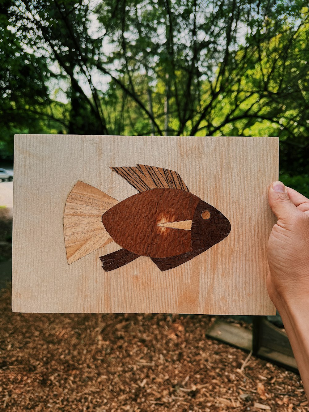 a hand holding a piece of wood with a fish on it