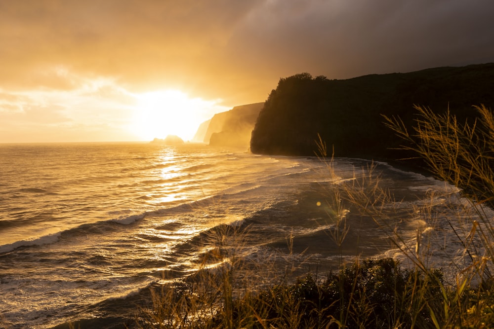 the sun is setting over the ocean on a cloudy day