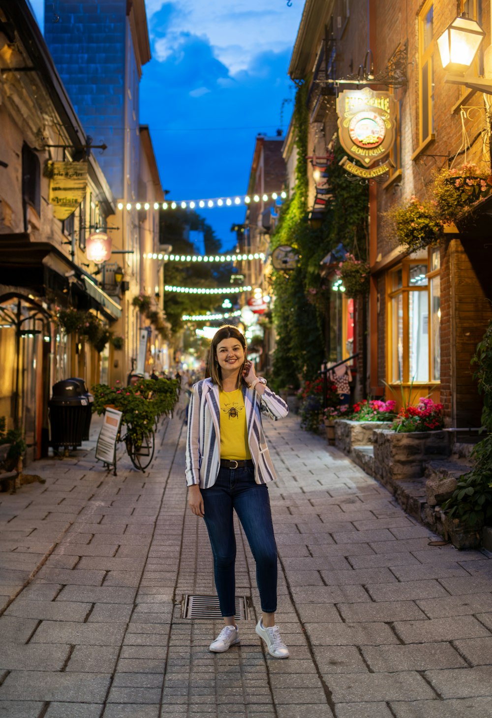 a woman standing on a brick street talking on a cell phone