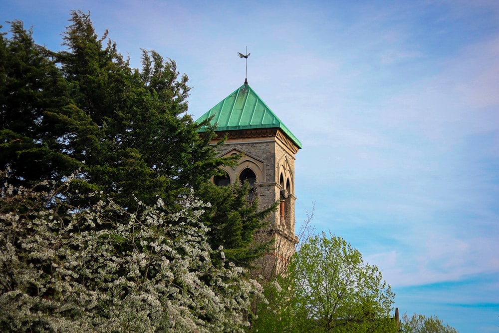 a tall tower with a green roof surrounded by trees
