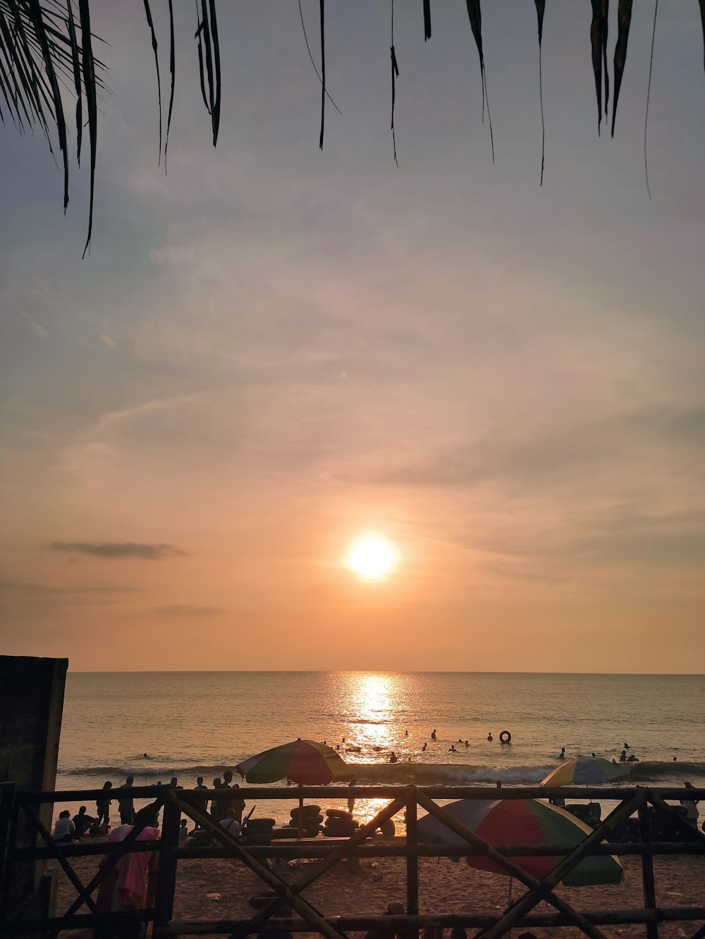 the sun is setting over the beach with umbrellas