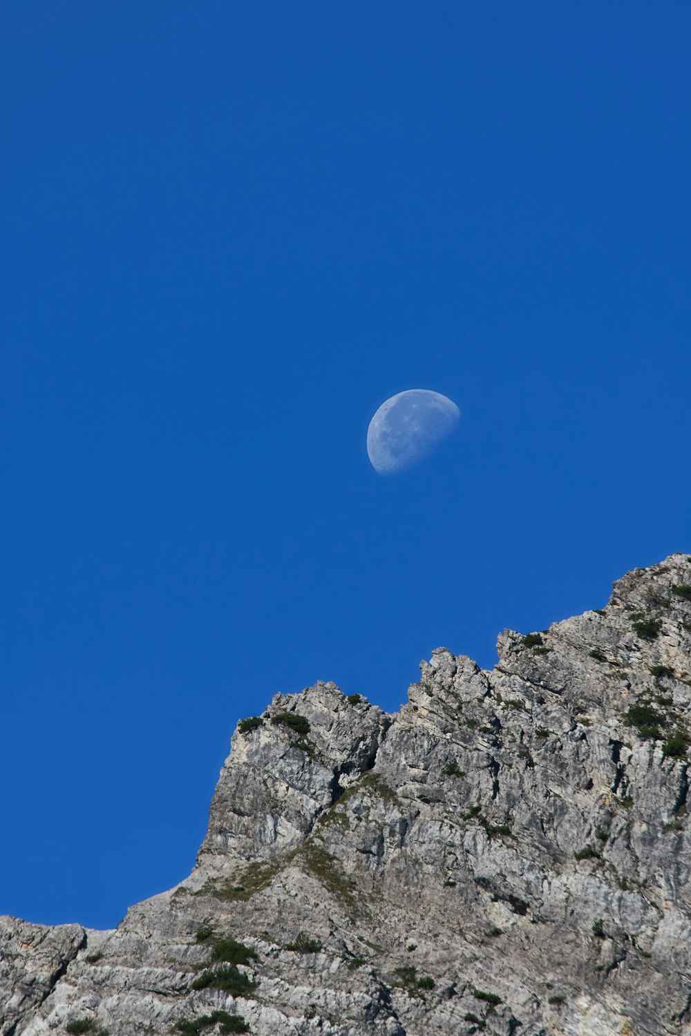 the moon is visible in the blue sky above a mountain