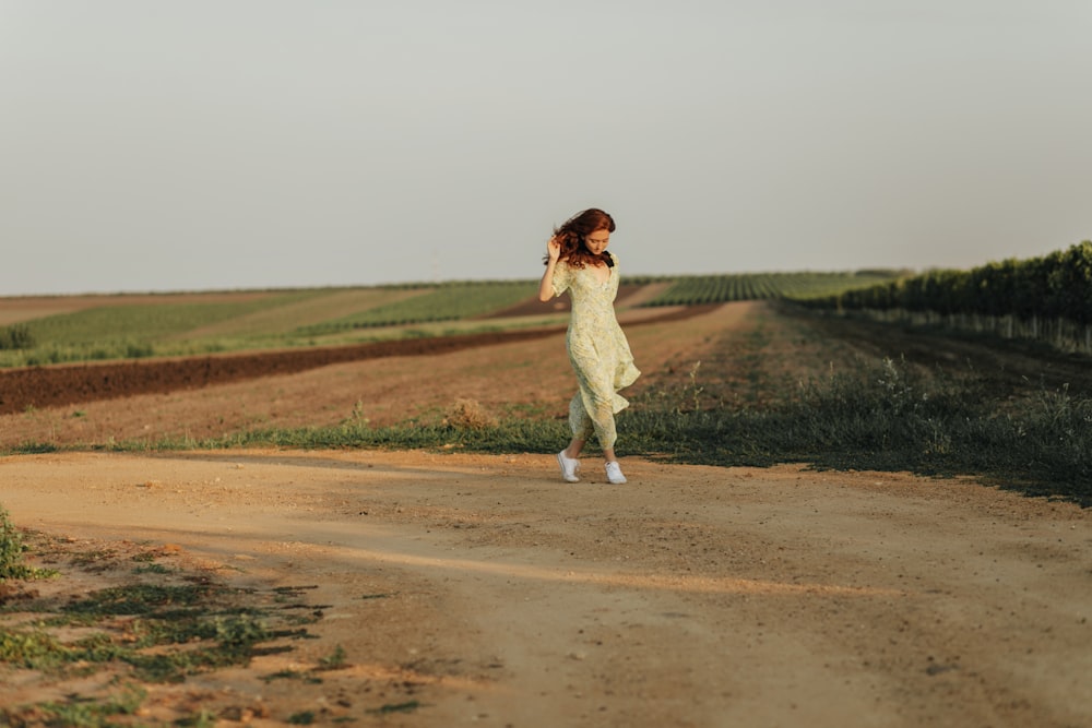 a woman in a white dress walking down a dirt road