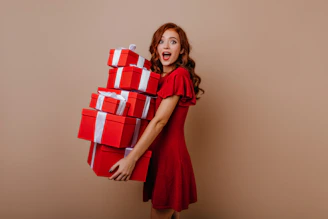 a woman in a red dress is holding a stack of presents