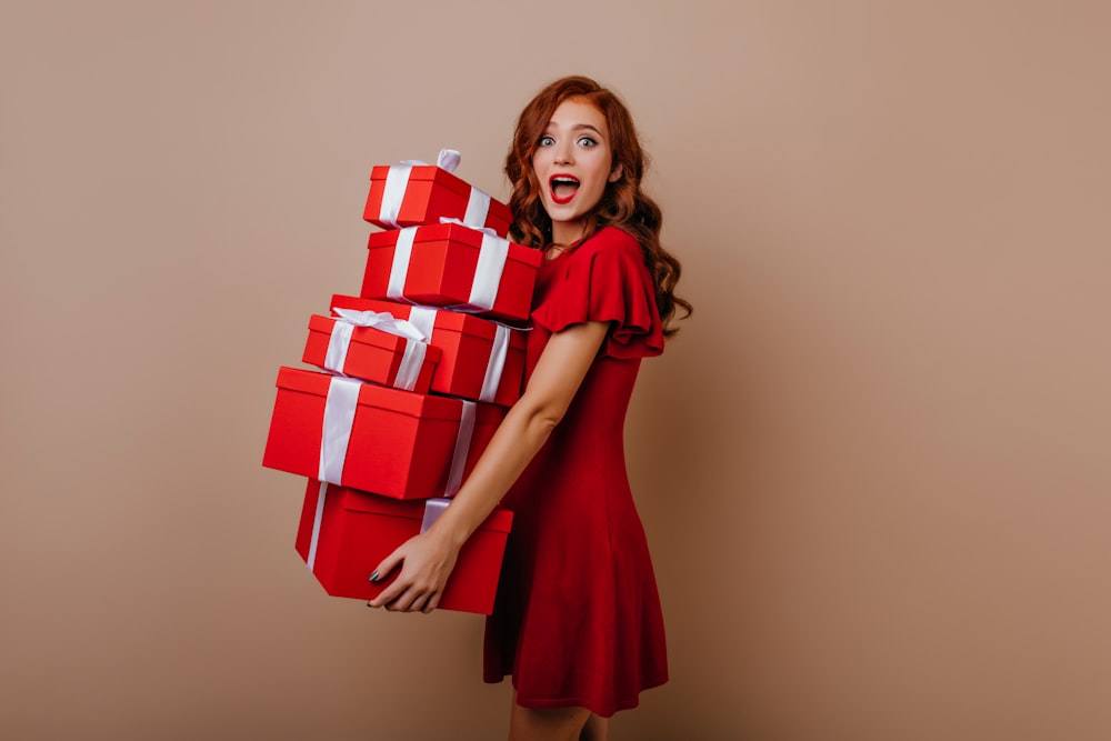 a woman in a red dress is holding a stack of presents