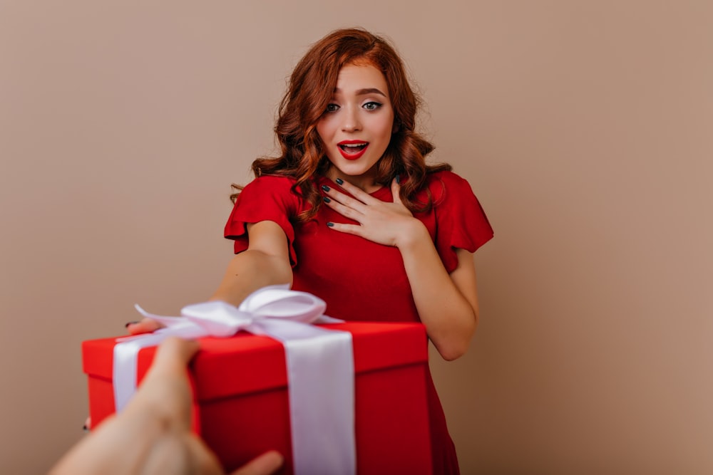 a woman in a red dress holding a red gift box