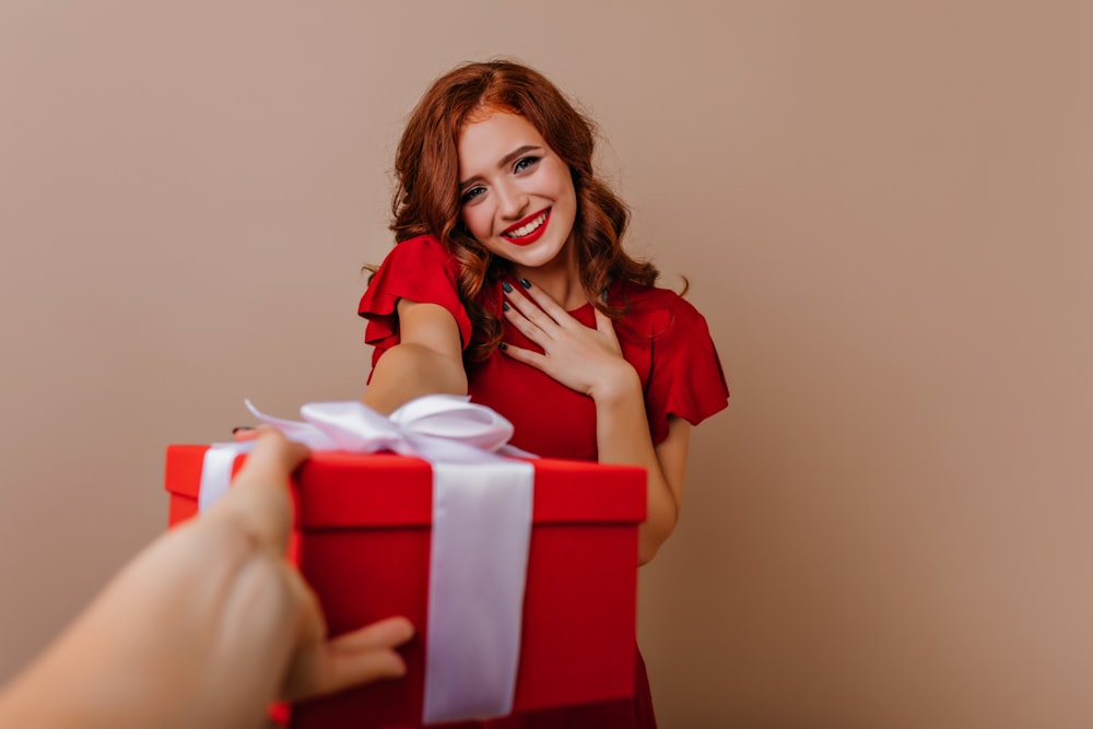 a woman holding a red gift box with a white ribbon